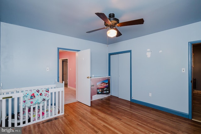 bedroom featuring wood-type flooring, a nursery area, a closet, and ceiling fan