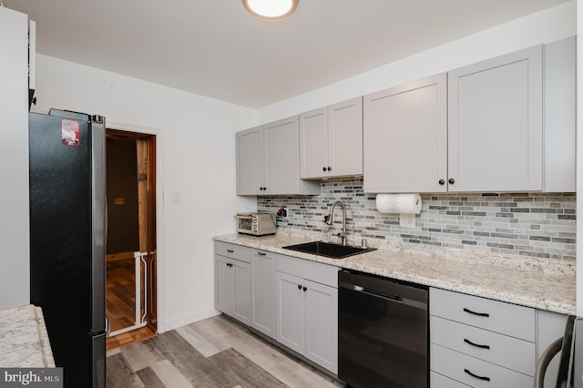 kitchen with appliances with stainless steel finishes, light wood-type flooring, backsplash, light stone counters, and sink