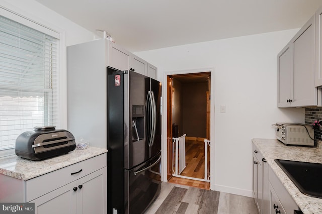 kitchen featuring backsplash, light stone counters, sink, light hardwood / wood-style flooring, and stainless steel fridge with ice dispenser