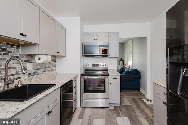 kitchen with light stone countertops, backsplash, stainless steel appliances, sink, and light hardwood / wood-style floors