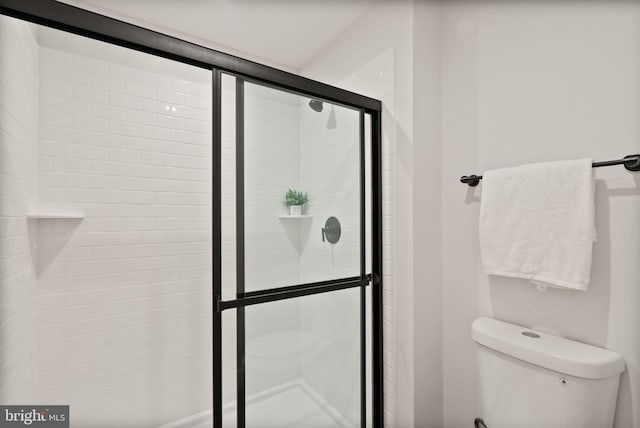 bathroom featuring a shower with door and toilet