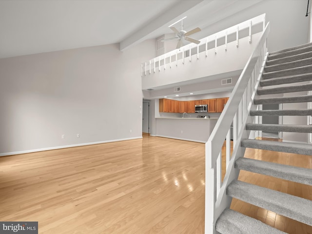 staircase with hardwood / wood-style flooring, ceiling fan, vaulted ceiling with beams, and sink