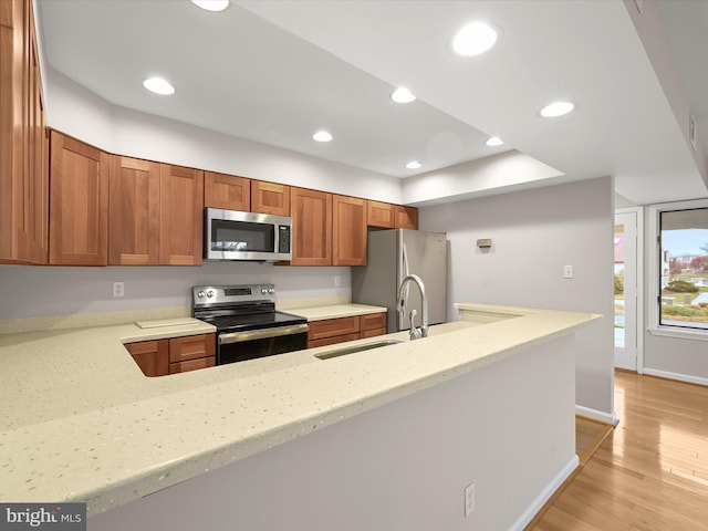 kitchen featuring kitchen peninsula, appliances with stainless steel finishes, light stone counters, sink, and light hardwood / wood-style flooring