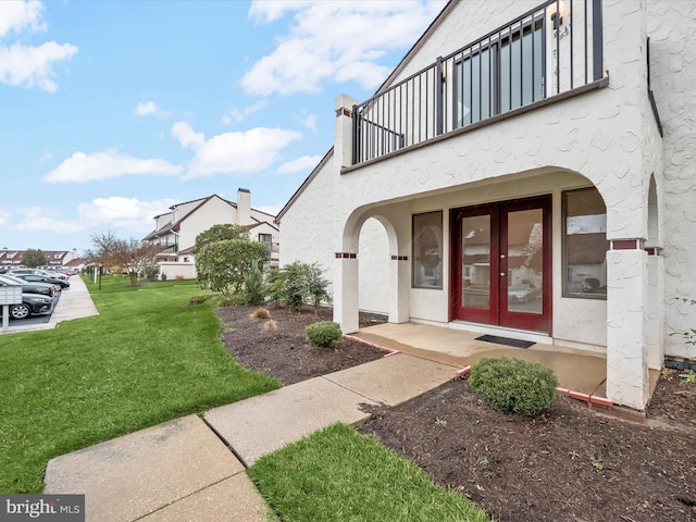 entrance to property with a balcony, a yard, and french doors