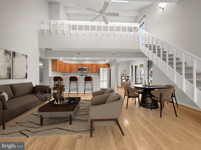 living room featuring ceiling fan, light hardwood / wood-style floors, and a towering ceiling