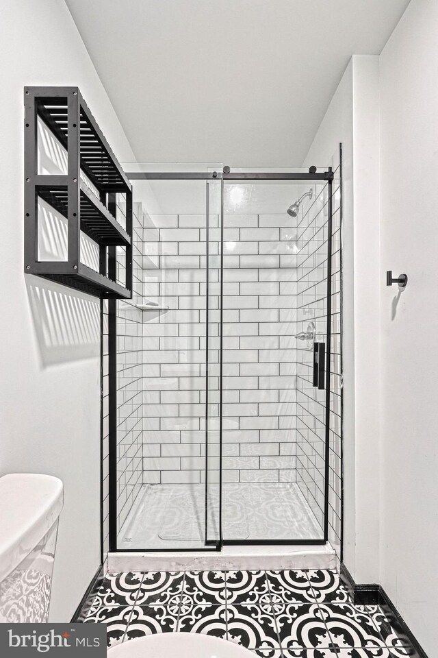 bathroom featuring toilet, a shower with door, and tile patterned floors