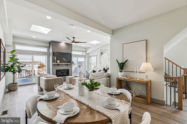 dining area featuring visible vents, a large fireplace, stairway, a skylight, and wood finished floors