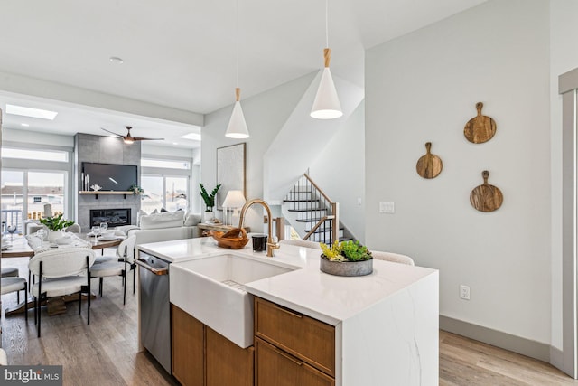 kitchen with a tiled fireplace, a sink, light wood-style floors, pendant lighting, and dishwasher