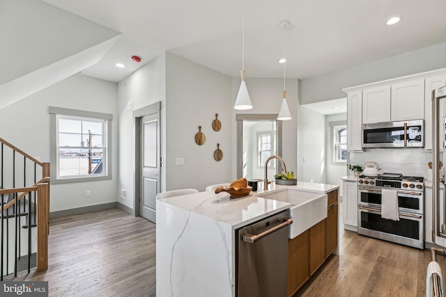 kitchen featuring a sink, decorative light fixtures, light stone counters, wood finished floors, and appliances with stainless steel finishes