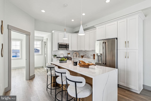 kitchen featuring a breakfast bar, an island with sink, appliances with stainless steel finishes, wood finished floors, and white cabinets