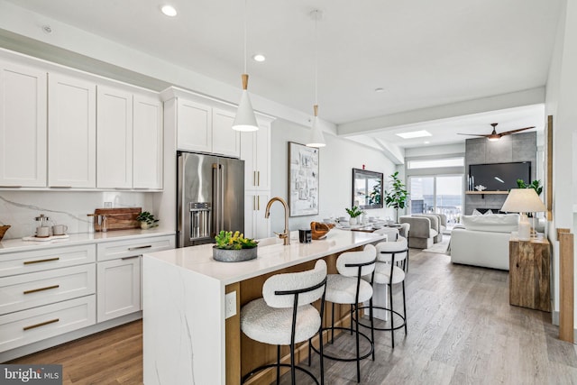 kitchen featuring wood finished floors, white cabinets, an island with sink, and high quality fridge