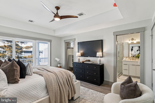 bedroom featuring visible vents, baseboards, light wood-style floors, and a tray ceiling