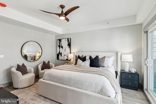 bedroom featuring a ceiling fan, a tray ceiling, wood finished floors, and baseboards