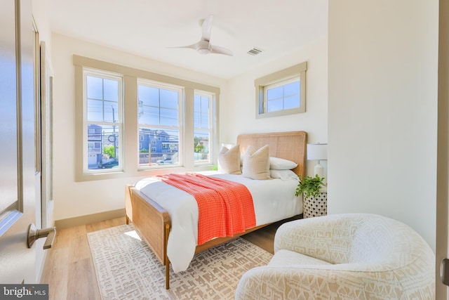 bedroom with ceiling fan, visible vents, baseboards, and wood finished floors