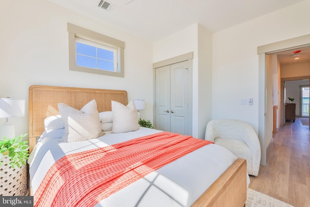 bedroom with light wood-style flooring, visible vents, and a closet