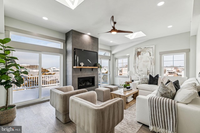 living area with wood finished floors, a skylight, a fireplace, recessed lighting, and ceiling fan