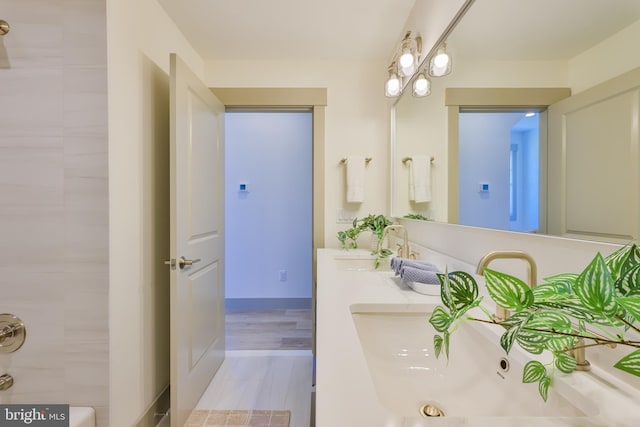 full bath featuring double vanity, wood finished floors, and a sink