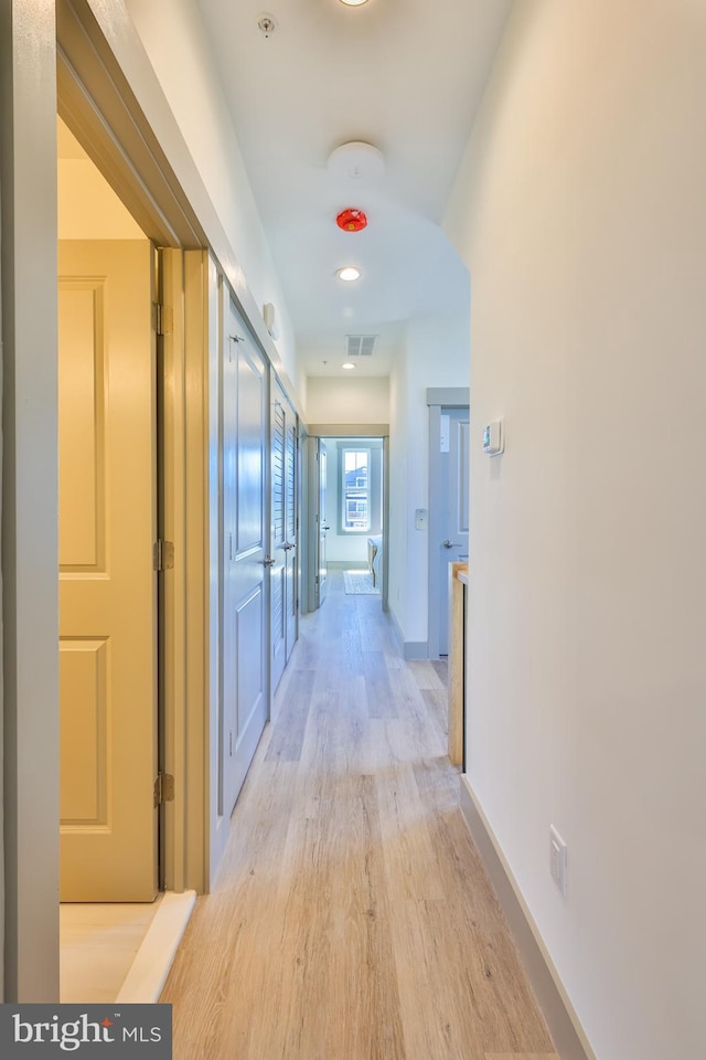 corridor featuring visible vents, baseboards, and light wood finished floors