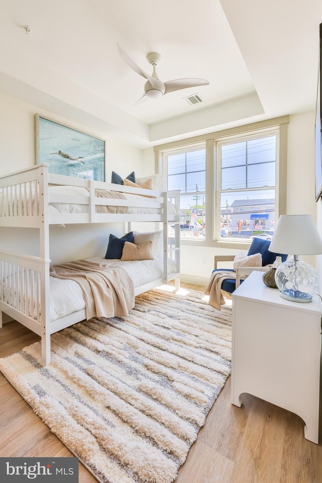 bedroom featuring ceiling fan, visible vents, a raised ceiling, and wood finished floors