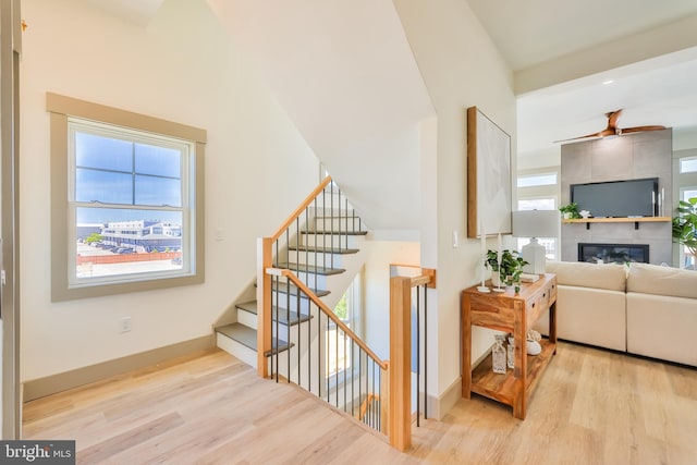 stairway featuring a healthy amount of sunlight, a fireplace, baseboards, and wood finished floors