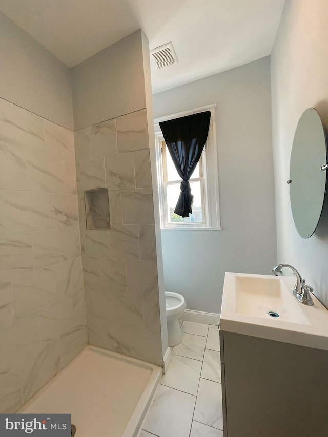 bathroom with a tile shower, tile patterned flooring, vanity, and toilet