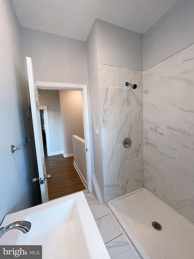 bathroom with wood-type flooring, a tile shower, and sink