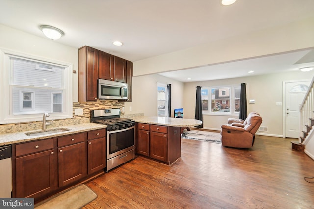 kitchen featuring sink, kitchen peninsula, stainless steel appliances, dark wood-type flooring, and light stone counters