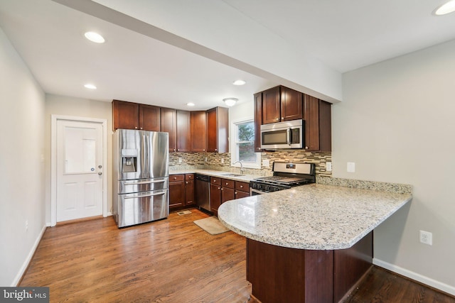 kitchen featuring kitchen peninsula, appliances with stainless steel finishes, hardwood / wood-style flooring, light stone countertops, and sink