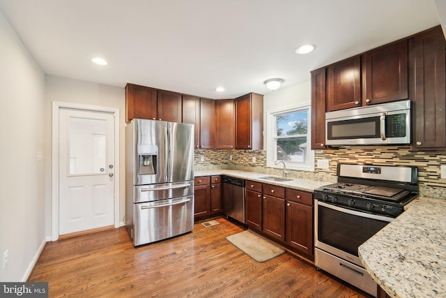 kitchen featuring decorative backsplash, stainless steel appliances, sink, light stone countertops, and dark hardwood / wood-style flooring