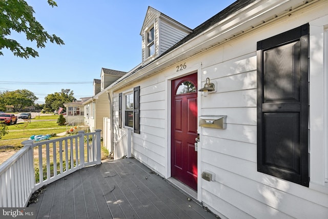 view of exterior entry with a wooden deck and a lawn