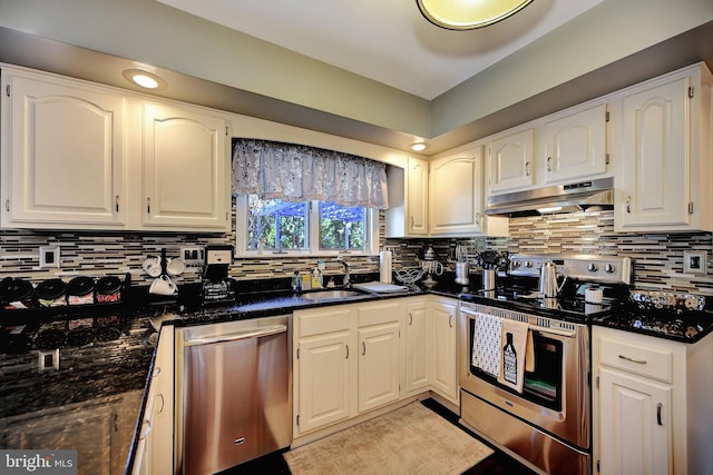 kitchen with dark stone counters, stainless steel appliances, white cabinetry, and backsplash