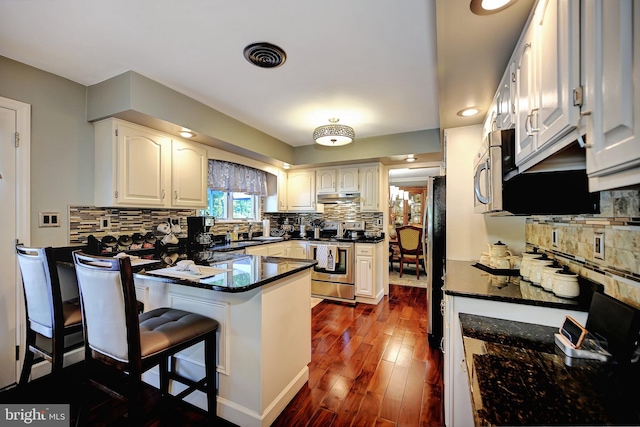 kitchen featuring dark wood-type flooring, white cabinets, kitchen peninsula, a kitchen bar, and appliances with stainless steel finishes