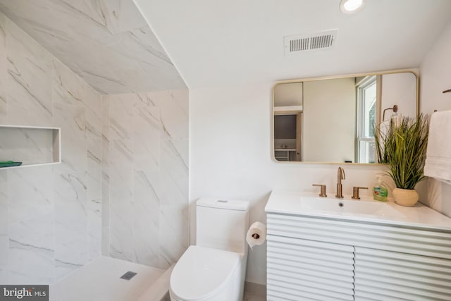 bathroom featuring a tile shower, vanity, and toilet