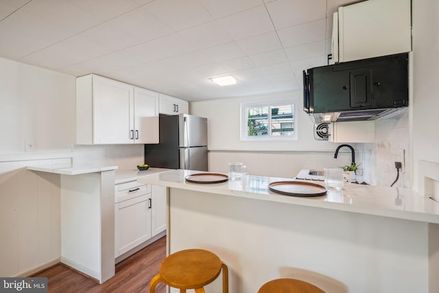 kitchen featuring a breakfast bar, sink, white cabinets, kitchen peninsula, and stainless steel refrigerator