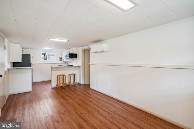 kitchen featuring stainless steel fridge, dark wood-type flooring, white cabinets, kitchen peninsula, and an AC wall unit