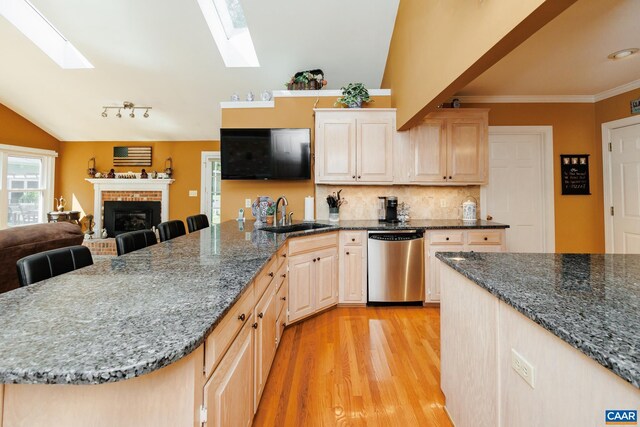 kitchen with lofted ceiling with skylight, dishwasher, light hardwood / wood-style floors, sink, and a brick fireplace