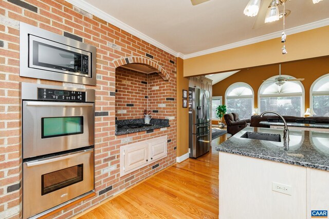 kitchen featuring crown molding, light wood-type flooring, stainless steel appliances, sink, and dark stone counters