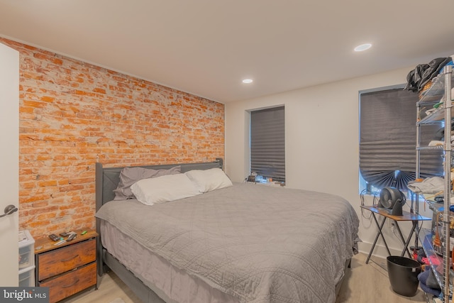 bedroom with light hardwood / wood-style floors and brick wall