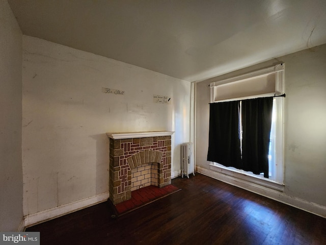 unfurnished living room with a stone fireplace, dark wood-type flooring, and radiator