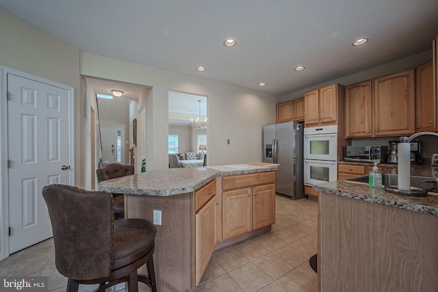 kitchen featuring a chandelier, a kitchen bar, a kitchen island, appliances with stainless steel finishes, and light tile patterned floors