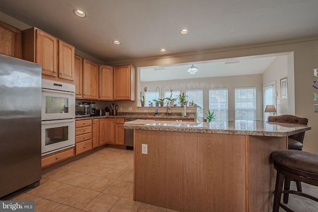 kitchen with appliances with stainless steel finishes, kitchen peninsula, light tile patterned floors, a kitchen bar, and sink