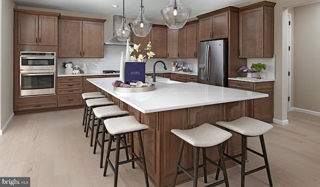 kitchen featuring light hardwood / wood-style flooring, stainless steel appliances, a kitchen island with sink, and a breakfast bar