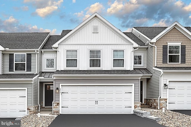 view of property featuring aphalt driveway, stone siding, board and batten siding, and an attached garage