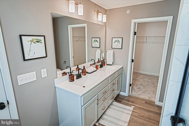 full bath featuring double vanity, wood finished floors, baseboards, and a sink