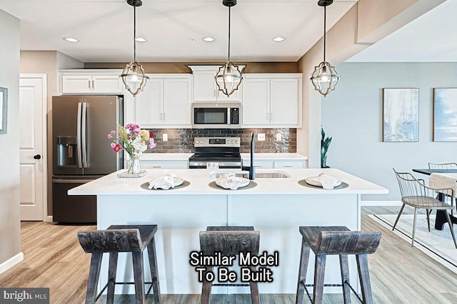 kitchen featuring white cabinetry, a kitchen island with sink, a sink, stainless steel appliances, and a kitchen bar