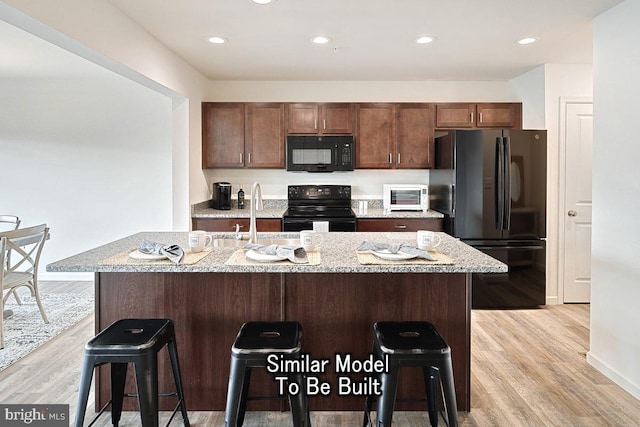 kitchen featuring a sink, light wood-style flooring, black appliances, and an island with sink