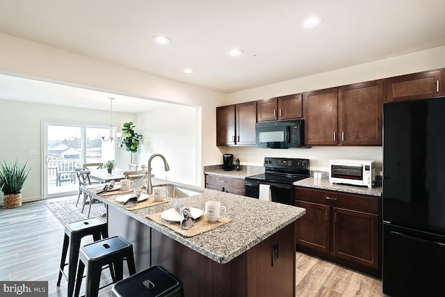 kitchen featuring light stone countertops, a breakfast bar area, light wood-style flooring, black appliances, and a sink