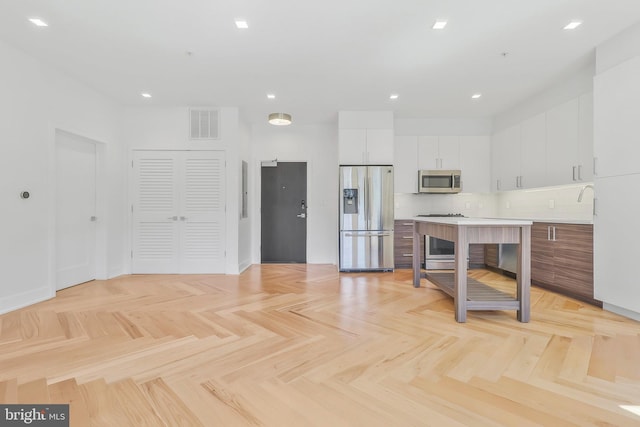 kitchen featuring light parquet floors, stainless steel appliances, decorative backsplash, and white cabinetry