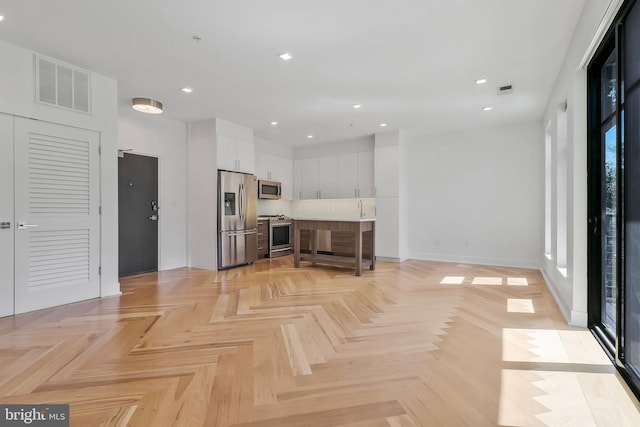 kitchen with light parquet flooring, white cabinets, appliances with stainless steel finishes, and a breakfast bar