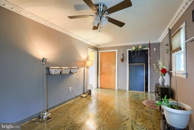 interior space with crown molding, wood finished floors, baseboards, and ceiling fan